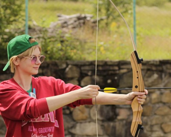 A young adult practicing archery outdoors in a casual setting, focusing on technique.